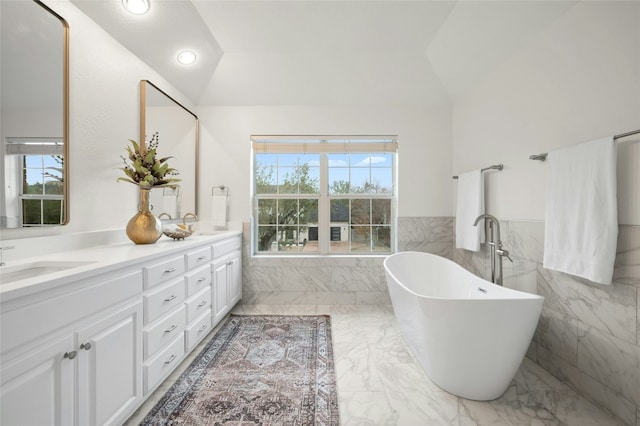 bathroom featuring vaulted ceiling, a bath, vanity, and tile walls