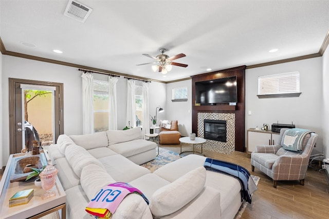 living room featuring ornamental molding, wood-type flooring, a large fireplace, and ceiling fan