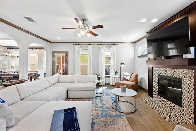 living area with arched walkways, a tile fireplace, light wood-style flooring, visible vents, and crown molding