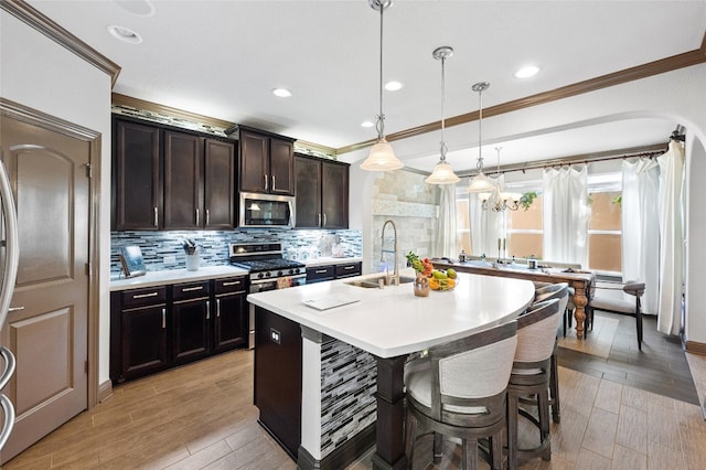 kitchen with sink, light wood-type flooring, pendant lighting, stainless steel appliances, and a kitchen island with sink