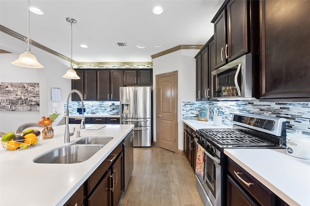 kitchen featuring a sink, light countertops, ornamental molding, appliances with stainless steel finishes, and hanging light fixtures