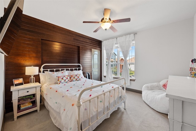 carpeted bedroom with ceiling fan, wooden walls, and baseboards