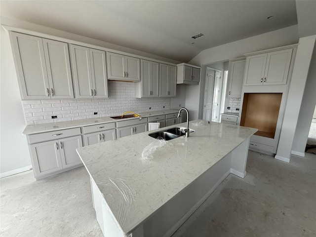 kitchen featuring light stone countertops, sink, and a center island with sink