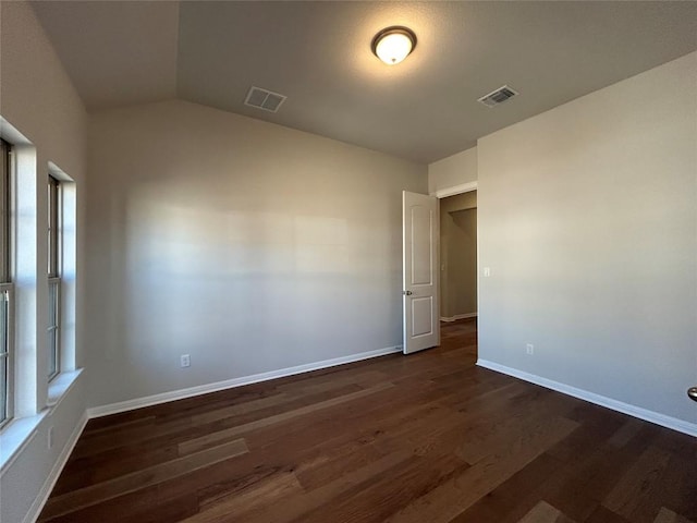 empty room featuring dark wood-style floors, baseboards, visible vents, and vaulted ceiling