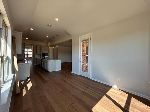 kitchen featuring visible vents, dark wood finished floors, oven, a kitchen island with sink, and a sink