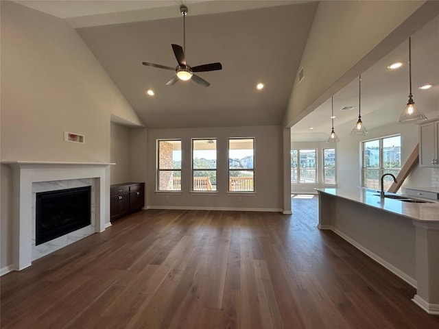 unfurnished living room with visible vents, dark wood-style flooring, high vaulted ceiling, a sink, and a high end fireplace