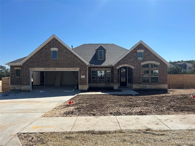 view of front of home with driveway, brick siding, stone siding, and fence