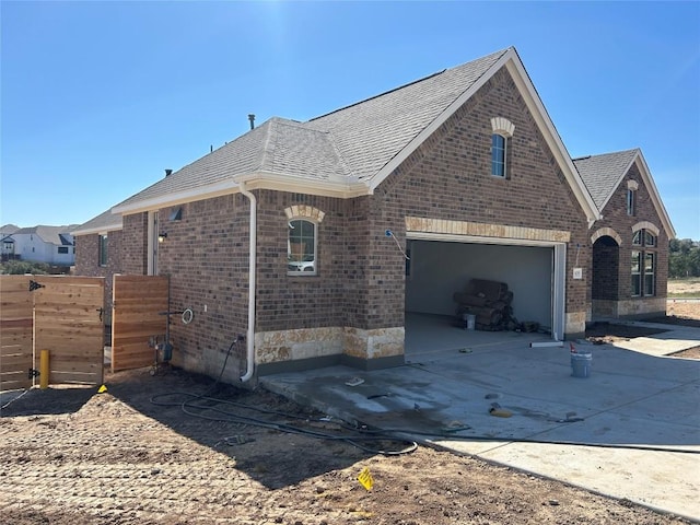 view of home's exterior featuring a garage, a shingled roof, concrete driveway, fence, and brick siding