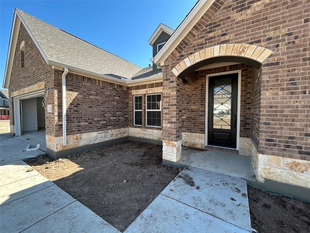 entrance to property with a garage, brick siding, and roof with shingles