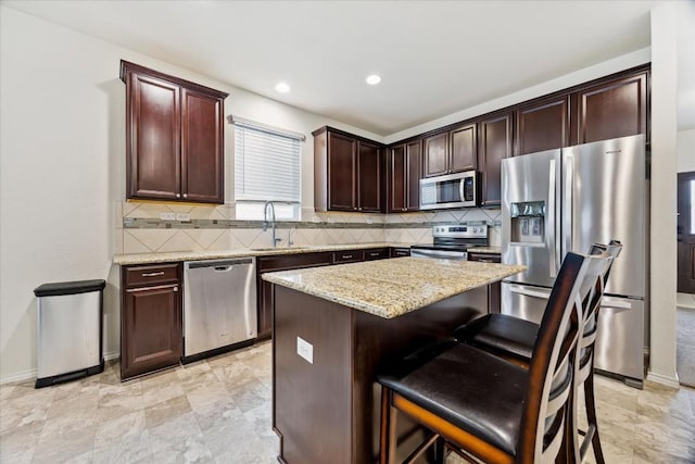 kitchen featuring sink, a kitchen breakfast bar, a kitchen island, stainless steel appliances, and light stone countertops