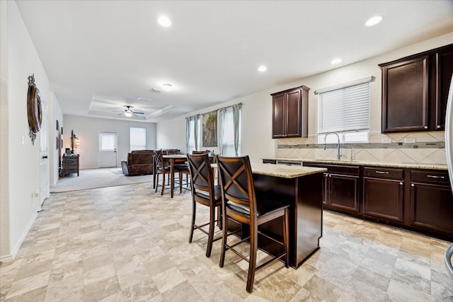 kitchen with sink, a breakfast bar area, backsplash, light stone counters, and a kitchen island