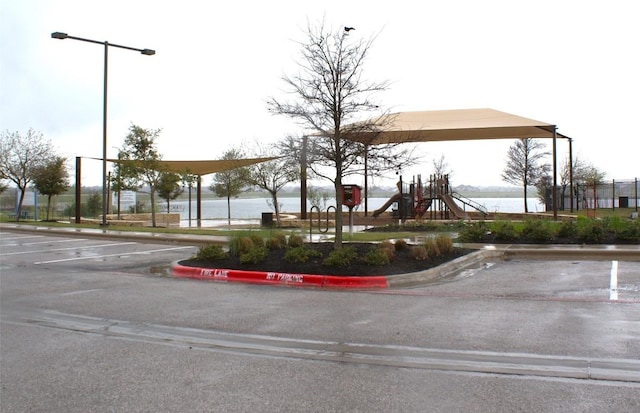 view of community featuring uncovered parking, playground community, and a water view