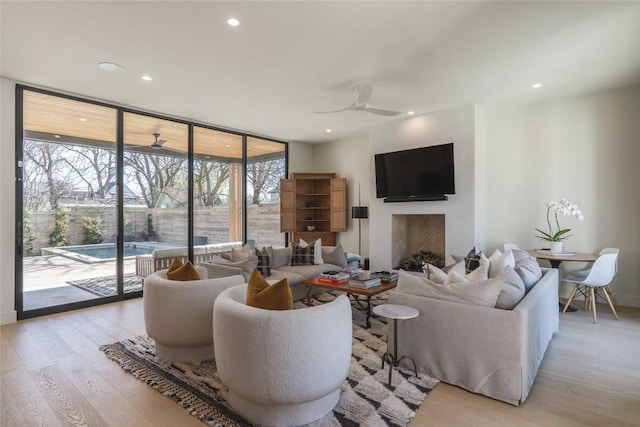 living room with ceiling fan, a wall of windows, and light hardwood / wood-style floors