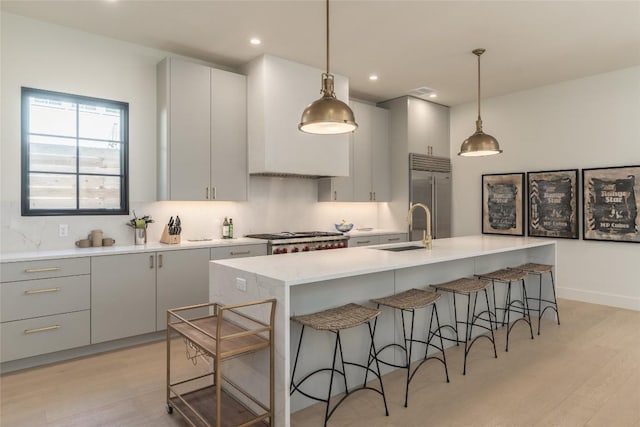 kitchen featuring stainless steel built in refrigerator, sink, range, an island with sink, and pendant lighting