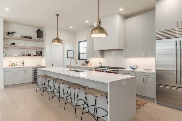 kitchen with wine cooler, sink, hanging light fixtures, stainless steel appliances, and a kitchen island with sink