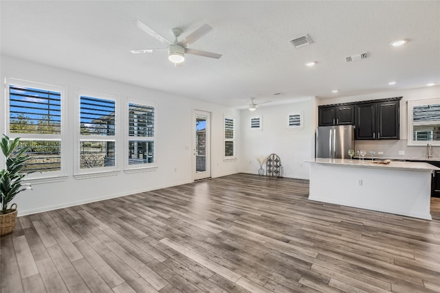 unfurnished living room featuring ceiling fan, sink, a textured ceiling, and light hardwood / wood-style flooring