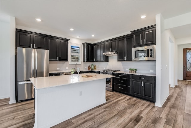 kitchen featuring an island with sink, appliances with stainless steel finishes, light wood-type flooring, and decorative backsplash