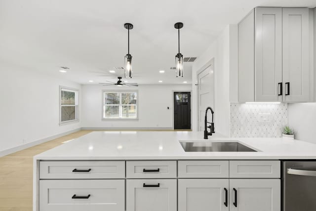 kitchen with dishwasher, sink, backsplash, hanging light fixtures, and light wood-type flooring