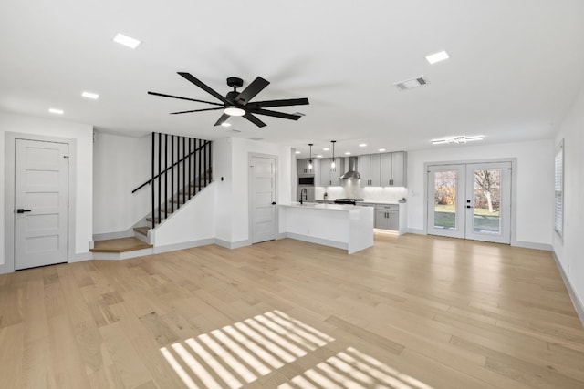 unfurnished living room with ceiling fan, sink, light wood-type flooring, and french doors