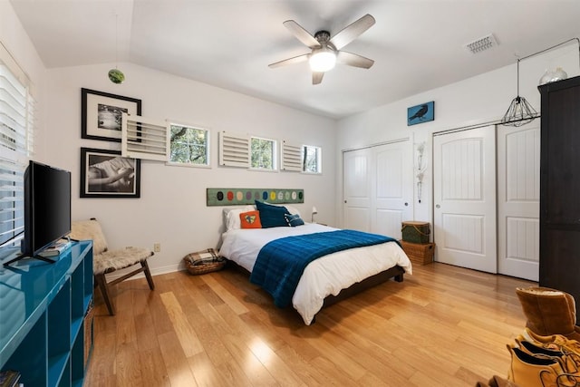 bedroom featuring lofted ceiling, two closets, wood-type flooring, and ceiling fan