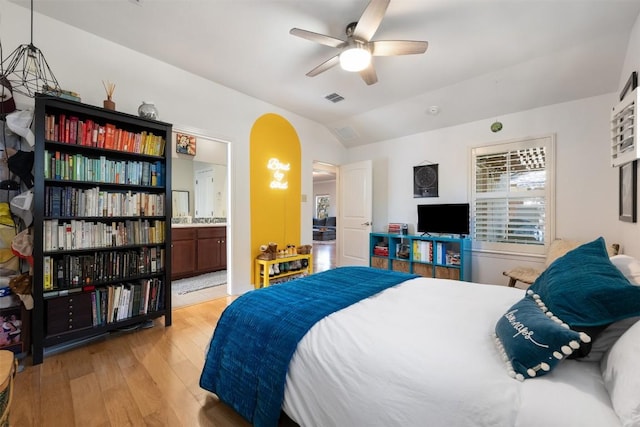 bedroom with visible vents, light wood-style flooring, arched walkways, vaulted ceiling, and connected bathroom