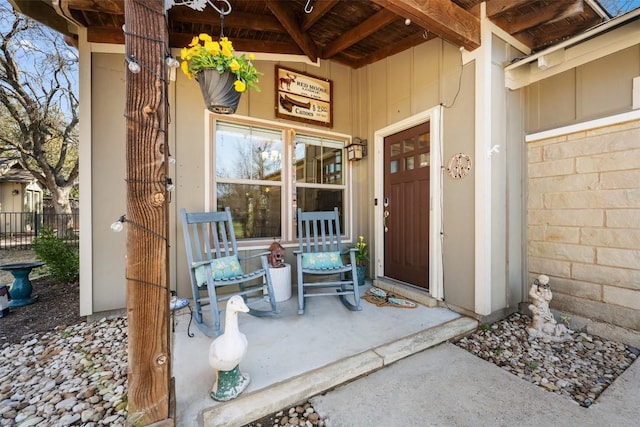 entrance to property featuring a porch, fence, and board and batten siding