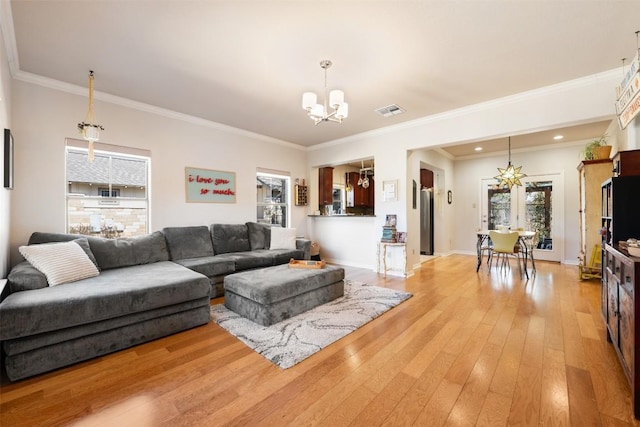 living room featuring baseboards, visible vents, light wood finished floors, ornamental molding, and a chandelier