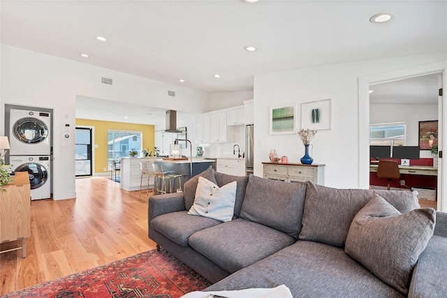 living room featuring lofted ceiling, stacked washer and dryer, sink, and light wood-type flooring