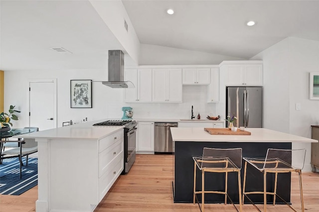 kitchen featuring range hood, white cabinetry, a breakfast bar area, a center island, and stainless steel appliances