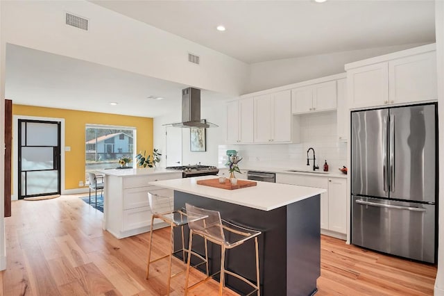 kitchen with sink, appliances with stainless steel finishes, a kitchen breakfast bar, island range hood, and a kitchen island