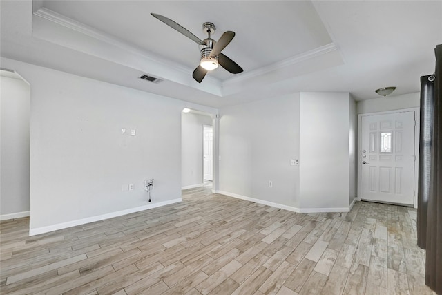 empty room with a tray ceiling, ornamental molding, and light wood-type flooring