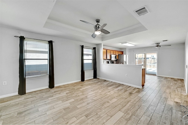 unfurnished room with a tray ceiling, plenty of natural light, ceiling fan, and light wood-type flooring