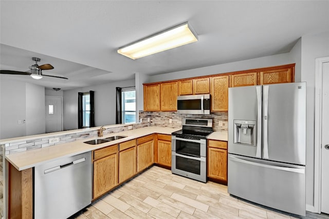 kitchen with sink, appliances with stainless steel finishes, light hardwood / wood-style floors, decorative backsplash, and kitchen peninsula