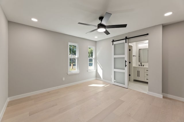 unfurnished bedroom with ceiling fan, connected bathroom, a barn door, and light hardwood / wood-style floors