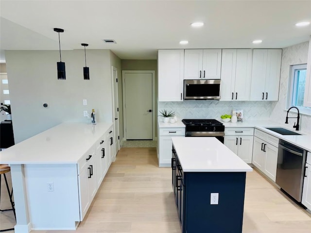 kitchen featuring pendant lighting, sink, appliances with stainless steel finishes, white cabinetry, and a center island