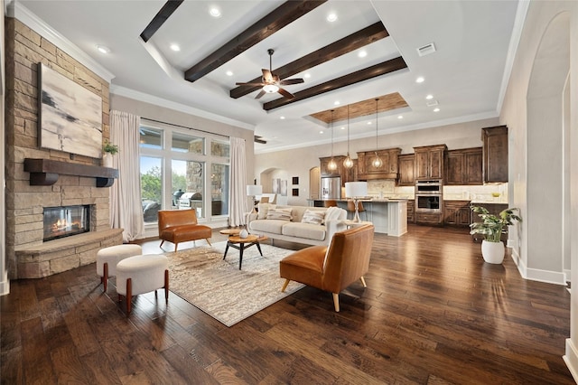 living room with dark wood-type flooring, a stone fireplace, ornamental molding, a tray ceiling, and beamed ceiling