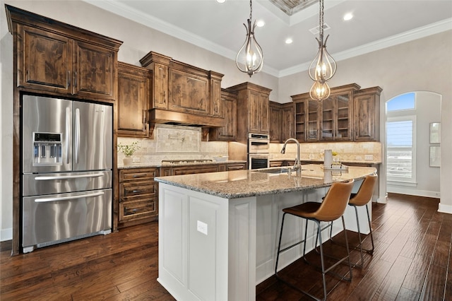 kitchen with an island with sink, sink, hanging light fixtures, ornamental molding, and stainless steel appliances