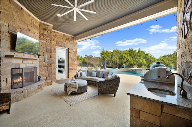 view of patio / terrace featuring sink, ceiling fan, an outdoor stone fireplace, and exterior kitchen