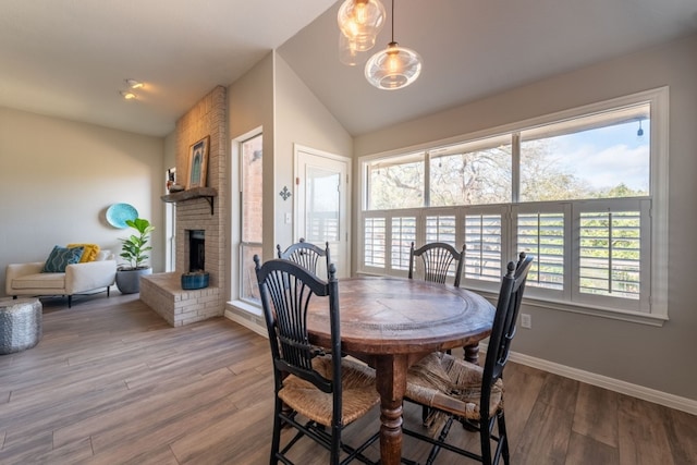 dining space with wood-type flooring, vaulted ceiling, and a brick fireplace