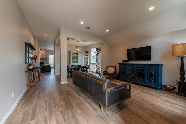 living room with lofted ceiling, wood-type flooring, and an inviting chandelier