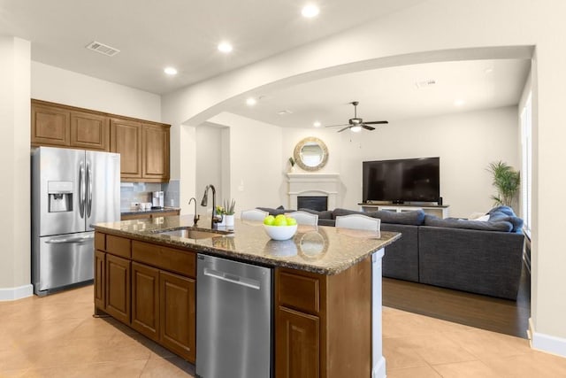 kitchen featuring dark stone countertops, sink, stainless steel appliances, and an island with sink