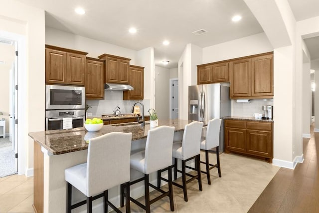 kitchen featuring a breakfast bar, sink, tasteful backsplash, stainless steel appliances, and a kitchen island with sink