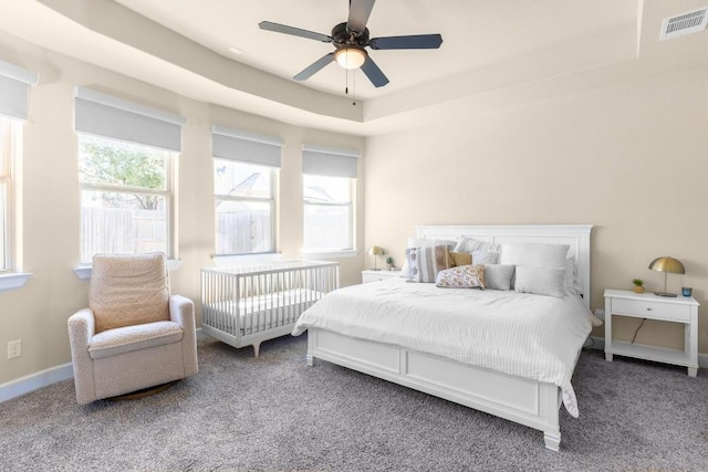 carpeted bedroom featuring a tray ceiling and ceiling fan