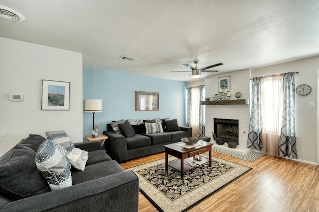 living room featuring ceiling fan, a textured ceiling, light hardwood / wood-style floors, and a fireplace