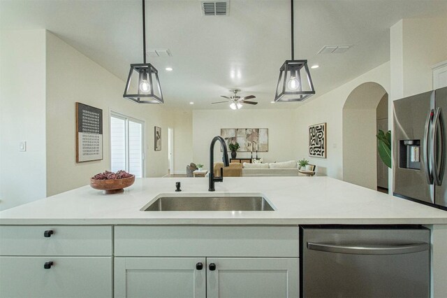 kitchen with decorative light fixtures, an island with sink, sink, white cabinets, and stainless steel appliances