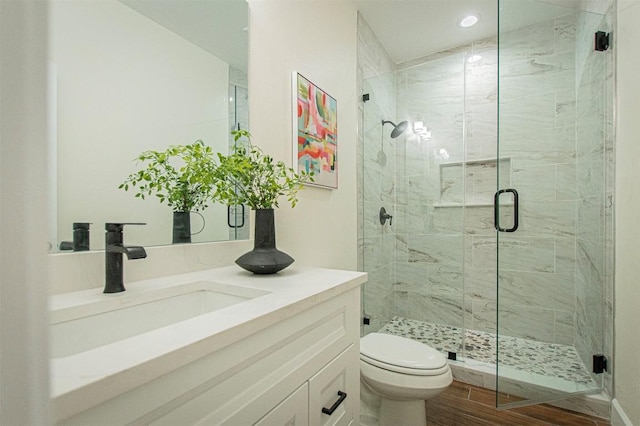 bathroom with wood-type flooring, toilet, a shower with shower door, and vanity