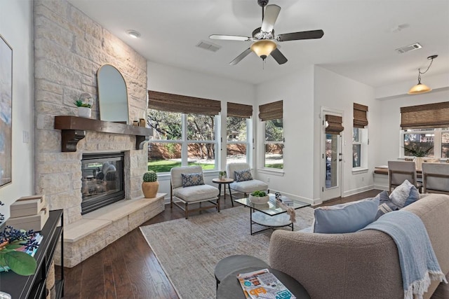 living room featuring a stone fireplace, dark wood-type flooring, and ceiling fan