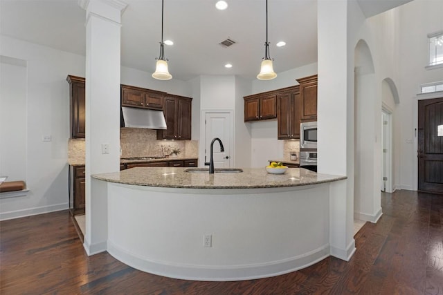 kitchen with dark wood-type flooring, sink, light stone counters, hanging light fixtures, and stainless steel appliances