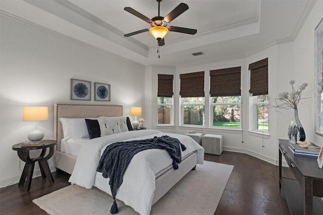 bedroom featuring dark hardwood / wood-style flooring, a tray ceiling, ornamental molding, and ceiling fan