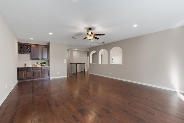 unfurnished living room featuring dark wood-type flooring, ceiling fan, and bar area